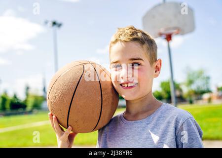 Jeune garçon jouant au basket-ball l'été Banque D'Images