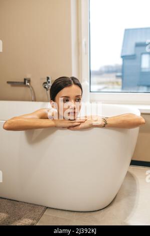 Femme attentionnés et peu animée assise dans la salle de bains Banque D'Images