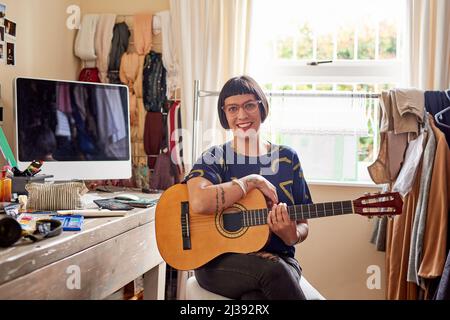 Elle a de la musique dans son âme. Portrait d'une jeune femme élégante assise dans sa salle éclectique jouant une guitare. Banque D'Images