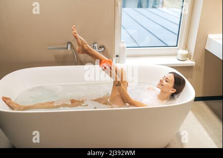 Une femme joyeuse se lavant avec un loofah savonneux Banque D'Images