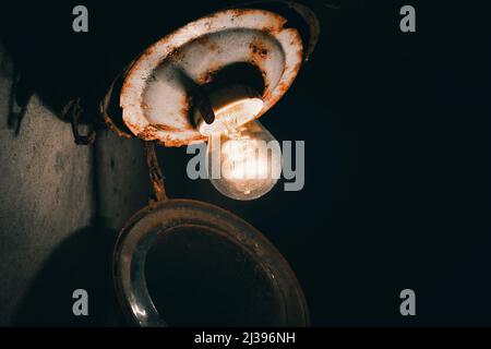 Une vieille ampoule à incandescence brille dans le sous-sol dans une ancienne nuance de verre avec une base rouillée Banque D'Images