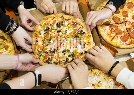 Vue de dessus, beaucoup d'amis, mains atteignant pour une tranche de pizza sur la table Banque D'Images