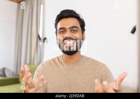 Portrait d'un jeune homme indien heureux assis à un bureau et en faisant des gestes. Un homme ethnique souriant impliquait une réunion virtuelle. Étudiant hispanique de sexe masculin participant à une conférence éducative Banque D'Images