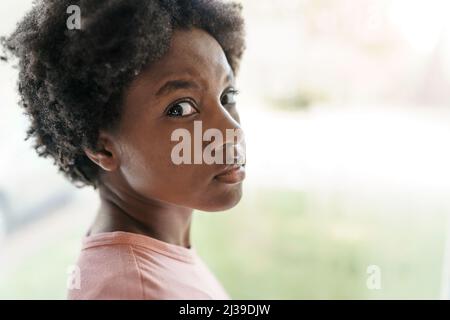 Une jeune femme afro-américaine pensive et triste regarde dans la fenêtre Banque D'Images