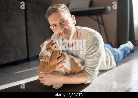 Homme jouant avec le chien d'animal de compagnie de basset à la maison sur son appartement Banque D'Images