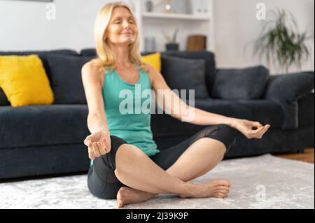 Santé et bien-être. Paisible et calme femme senior pratiquant le yoga à la maison, une femme plus âgée est assise en position lotus, femme d'âge moyen médite Banque D'Images