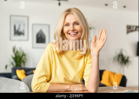 Une femme caucasienne, âgée et énergique, est prête pour un entretien en ligne lors d'un appel vidéo, assise à la réception et regardant et agitant la caméra, dit Bonjour. Concept de recherche d'emploi Banque D'Images