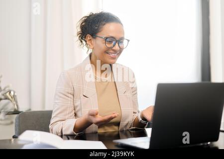 Concept de réunion vidéo. Une femme d'âge moyen gaie tenant un appel vidéo sur l'ordinateur portable au bureau, faisant un geste dans une webcam, discutant avec des interlocuteurs, impliquée dans une réunion vidéo en ligne avec l'équipe de travail Banque D'Images