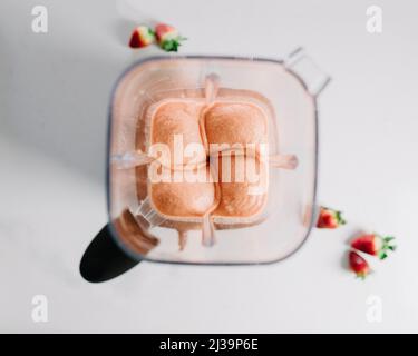 Un smoothie rose dans un blender avec des fraises Banque D'Images