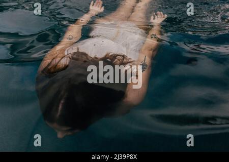 femme avec tatouages nager sous l'eau dans la piscine sombre Banque D'Images