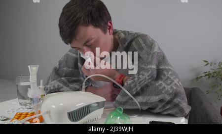 L'homme fait l'inhalation en utilisant un nébuliseur à la maison. Mâle traité indépendamment avec un inhalateur avec, médicament de pulvérisation pour les voies respiratoires supérieures et inférieures Banque D'Images