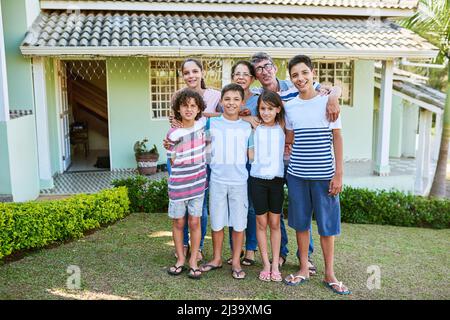 Cette maison a construit trois générations de souvenirs de famille. Portrait d'une famille heureuse de plusieurs générations debout ensemble dans leur arrière-cour. Banque D'Images