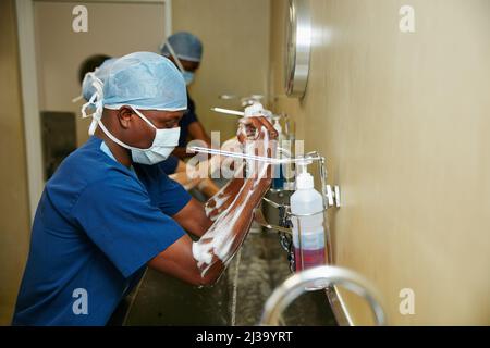 L'hygiène est de la plus haute importance. Cliché d'une équipe de chirurgiens stérilisant leurs bras et leurs mains dans le cadre d'une routine chirurgicale. Banque D'Images