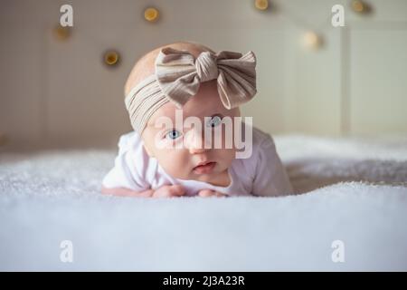 Bébé fille de 3 mois se trouve sur un lit avec des vêtements blancs sur son ventre et sourit, regarde la caméra, bébé matin, le concept de substance de bébé. Banque D'Images