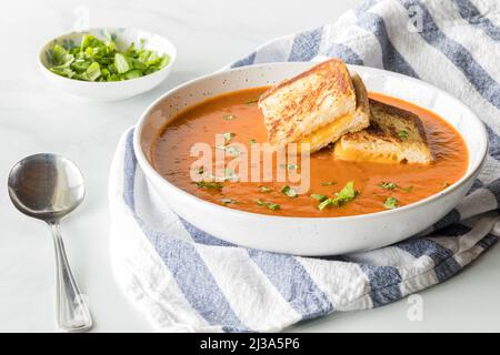 Un bol de soupe de tomates avec de petits sandwiches au fromage grillé comme garniture sur le dessus. Banque D'Images