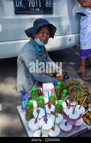 Une femme de rue vendeur assis sur le sol et vendant des boissons tamarin locales pendant une cérémonie au temple de Goa Lawah à Klungkung Regency, Bali. Banque D'Images