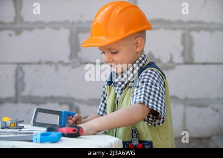 Portrait de petit constructeur en casques avec instruments pour la rénovation sur la construction. Garçon de créateur, enfant de menuisier avec ensemble d'outils de constructeur. Banque D'Images