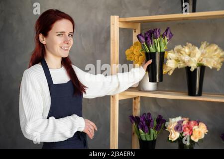 Petite entreprise. Femme fleuriste en fleuriste près de la vitrine avec tulipes. Studio de design floral, production de décorations et d'arrangements. Fleur Banque D'Images