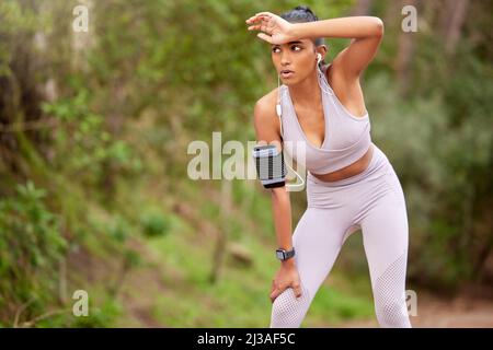 Il devient toujours dur à la fin. Photo d'une jeune femme prenant une pause tout en faisant du jogging dans la forêt. Banque D'Images