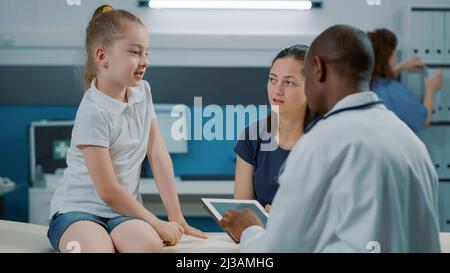 Petit enfant ayant une discussion avec un médecin de sexe masculin à l'examen au bureau médical. Enfant et médique parlant du diagnostic des soins de santé et du traitement de rétablissement lors de la visite de contrôle. Banque D'Images