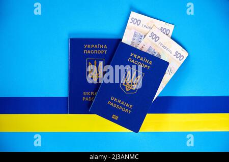 Deux passeports biométriques des citoyens ukrainiens et des hryvnias ukrainiens sur fond bleu avec un ruban jaune et bleu. Le concept de migration de U Banque D'Images