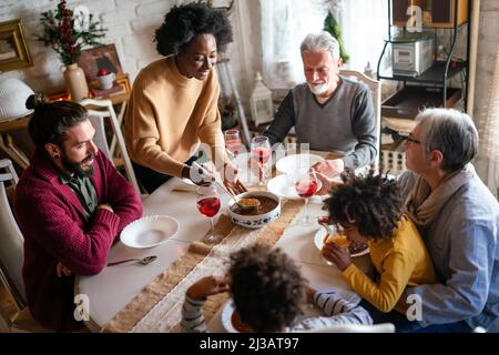 Bonne famille multiethnique multigénération s'amusant autour d'une table de cuisine. Banque D'Images