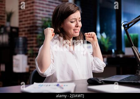 Jeune entrepreneur adulte enthousiaste et positif, enthousiaste, enthousiaste à l'idée d'un nouvel emploi au bureau la nuit. Bonne joyeuse jeune femme d'affaires adulte célébrant la fin du projet de démarrage avant la date limite. Banque D'Images