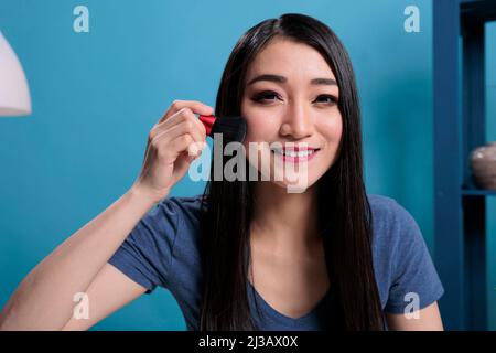 Portrait d'un influenceur asiatique qui fait un tutoriel de maquillage devant l'appareil photo tout en enregistrant le créateur de contenu pour le canal de vlogging. Vlogger femme utilisant la brosse de cosmétiques de la publicité de maquillage produit Banque D'Images