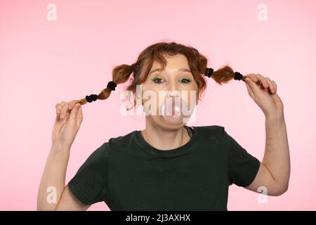 Bulle de gomme à mâcher. Jeune fille adolescente soufflant de gomme à bulles rose. Fille soufflant grande bulle isolé couleur rose fond Banque D'Images