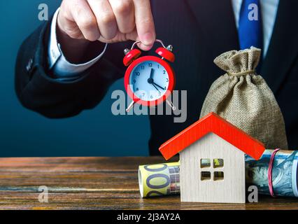 Agent immobilier tenant une horloge au-dessus de la maison. Offre limitée. Entreprise de location. Offres spéciales pour l'achat d'une maison. Faire un prêt hypothécaire. Solde saisonnier. Inpes Banque D'Images