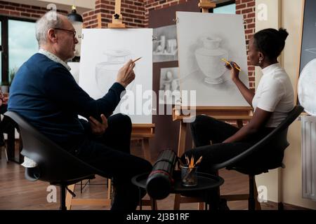 Professeur de peintre senior expliquant la leçon d'esquisse à un jeune étudiant pendant un cours d'art dans la leçon de créativité. Les étudiants dessinant le modèle de vase développant de nouvelles compétences pour la croissance personnelle Banque D'Images