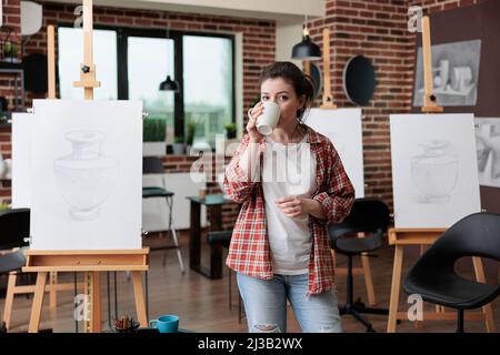 Portrait d'un professeur d'art debout dans un lieu de travail créatif boire du café avant de commencer à travailler à l'illustration du croquis à l'aide d'un crayon graphique. Jeune artiste développant des compétences artistiques pour la croissance personnelle Banque D'Images