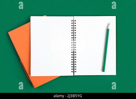 Carnet avec crayon. Ouvrez le bloc-notes sur fond vert foncé, le bloc-notes en spirale du bureau sur une table avec des pages vierges. Vue de dessus. Page blanche pour l'écriture. Banque D'Images