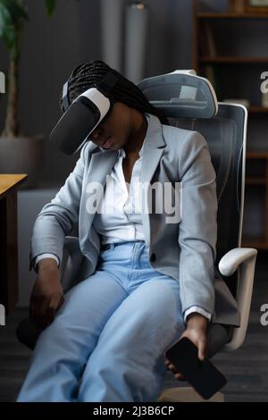 Femme d'affaires africaine fatiguée dormant en portant des lunettes vr avec un smartphone dans les mains au bureau au travail Banque D'Images