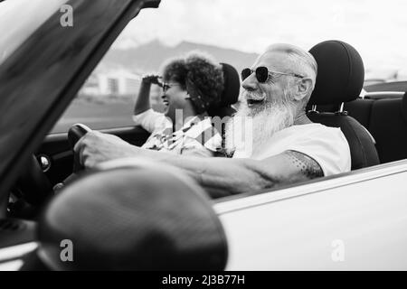 Joyeux couple senior s'amusant en voiture convertible pendant les vacances d'été - Focus sur le visage de l'homme - montage noir et blanc Banque D'Images