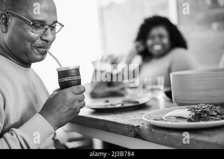 Heureux père noir buvant yerba mate pendant le déjeuner à la maison - foyer principal sur la tasse - montage noir et blanc Banque D'Images