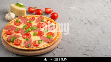 Ingrédients alimentaires et épices pour la cuisson du fromage mazarella, des tomates cerises, de l'ail, du basilic et de délicieuses pizzas italiennes sur fond de béton gris. Co Banque D'Images