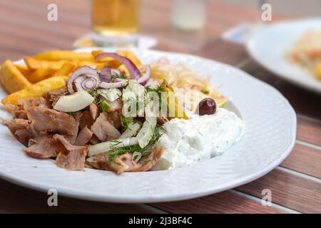 Repas grec Gyros de viande rôtie en tranches avec frites, oignons, coleslaw et tzatziki sur une assiette blanche dans un restaurant en plein air, gros plan, s Banque D'Images