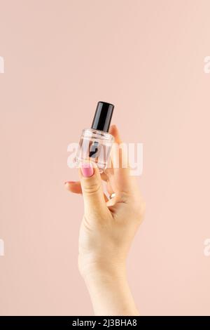 Une maquette d'une bouteille avec vernis à ongles transparent dans la main d'une femme sur fond rose. Concept de manucure. Banque D'Images