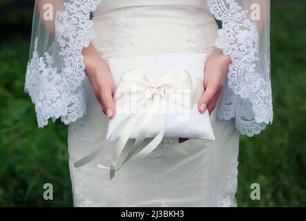 Anneaux de mariage sur coussin blanc dans les mains de la mariée. Mariée dans une robe de mariage blanche et un long voile tient dans ses mains classique anneau de mariage doré Banque D'Images