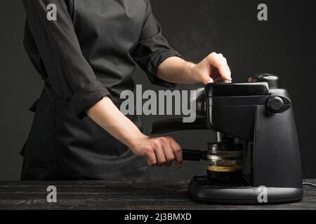 Un bariste professionnel avec une machine à café prépare du café. Sur fond sombre Banque D'Images