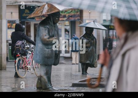 Hanovre, Allemagne. 07th avril 2022. Un passant passe passe devant les personnages de l'artiste Ulrike Enders avec un parapluie. Le Service météorologique allemand met en garde contre les orages, les orages et les fortes pluies. Crédit : OLE Spata/dpa/Alay Live News Banque D'Images