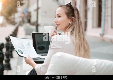 une femme d'affaires travaille sur un ordinateur portable tout en étant assise à une table dans un café extérieur. Banque D'Images