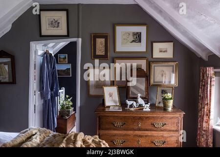 Des photos encadrées de dorures et une commode en bois dans la chambre à coucher mansardée du 18th siècle Suffolk Cottage, Royaume-Uni Banque D'Images