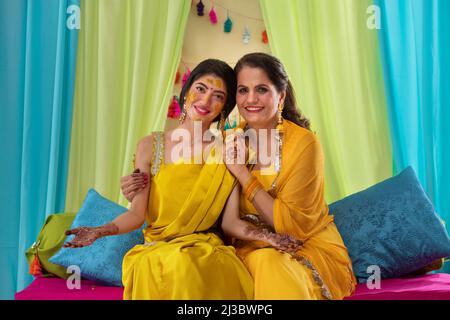 Mariée indienne assise à côté de sa mère et montrant ses paumes peintes avec mehndi lors de la cérémonie haldi Banque D'Images