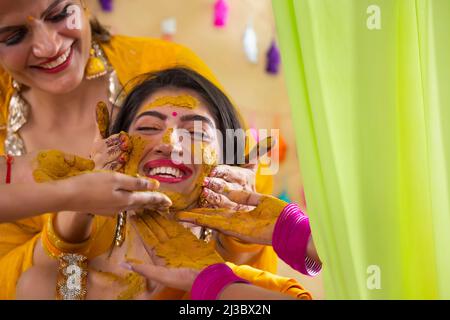 Mains de femmes appliquant de la pâte curcuma sur le visage de la mariée sur le rasam de haldi Banque D'Images