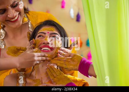 Mains de femmes appliquant de la pâte curcuma sur le visage de la mariée sur le rasam de haldi Banque D'Images