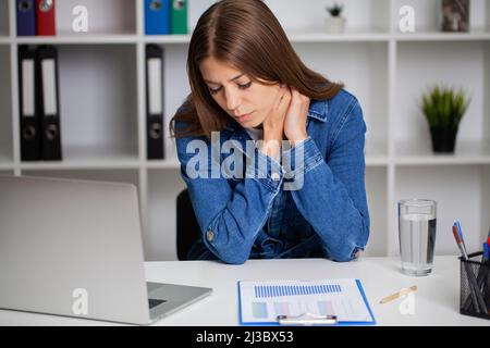 Jeune femme Moody tenant son cou au bureau Banque D'Images