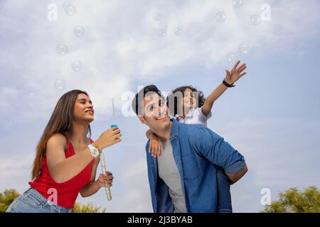 Parent heureux avec leur fils s'amusant avec des bulles volantes dans le parc Banque D'Images