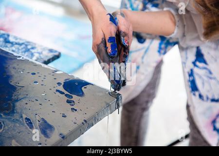 Gros plan des mains de l'artiste recouvertes de peinture utilisée pour la peinture sur toile, portant une couche blanche recouverte de peinture Banque D'Images